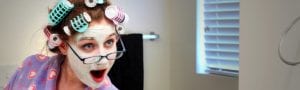 woman with her hair in curlers and a face mask singing into a brush