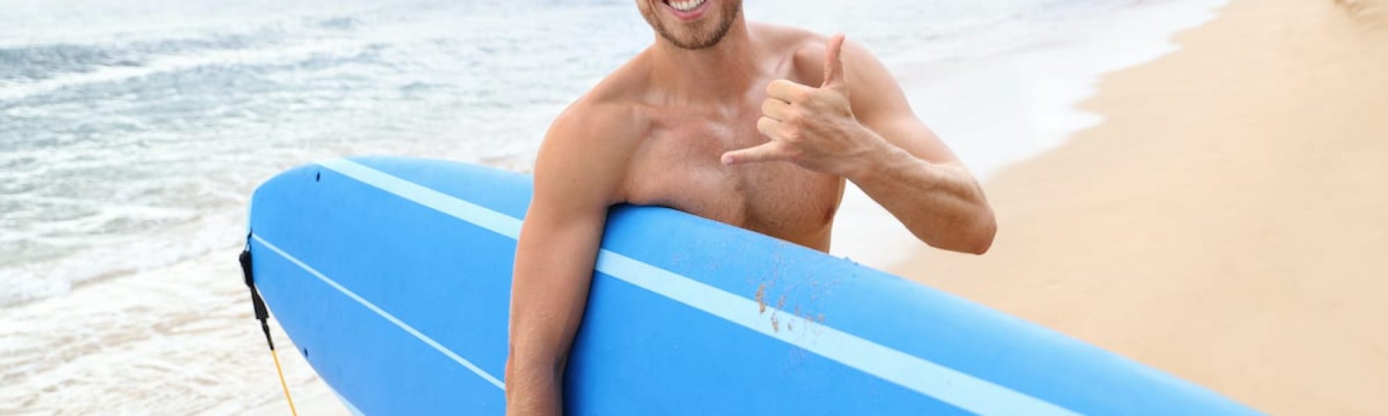 Surfer man surfing doing hawaii shaka surf sign Surfer guy happy with surf surfing smiling doing hawaiian shaka hand sign for fun during surf session in ocean waves on beach vacation. Surfing travel destination. Friendly greeting in surfer culture.