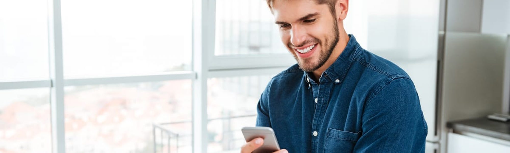 Young man using a smartphone and smiling indoors Picture of young man using a smartphone and smiling. Looking at smartphone.