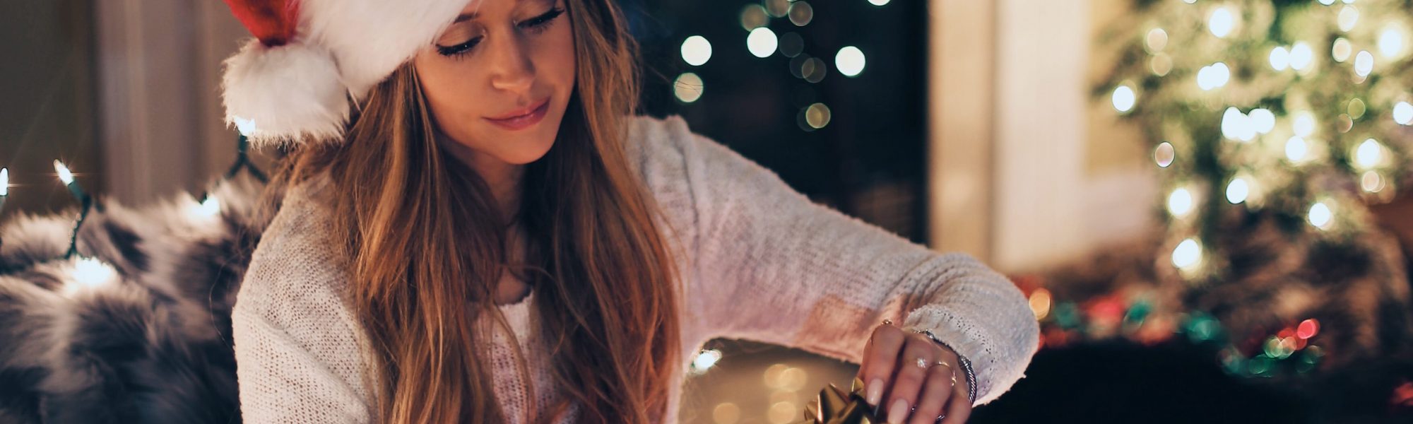 savingsguide lady in santa hat opening up presents by a christmas tree
